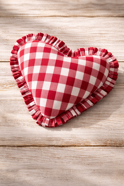 Heart-shaped red and white checkered pillow with ruffled edges on a wooden surface