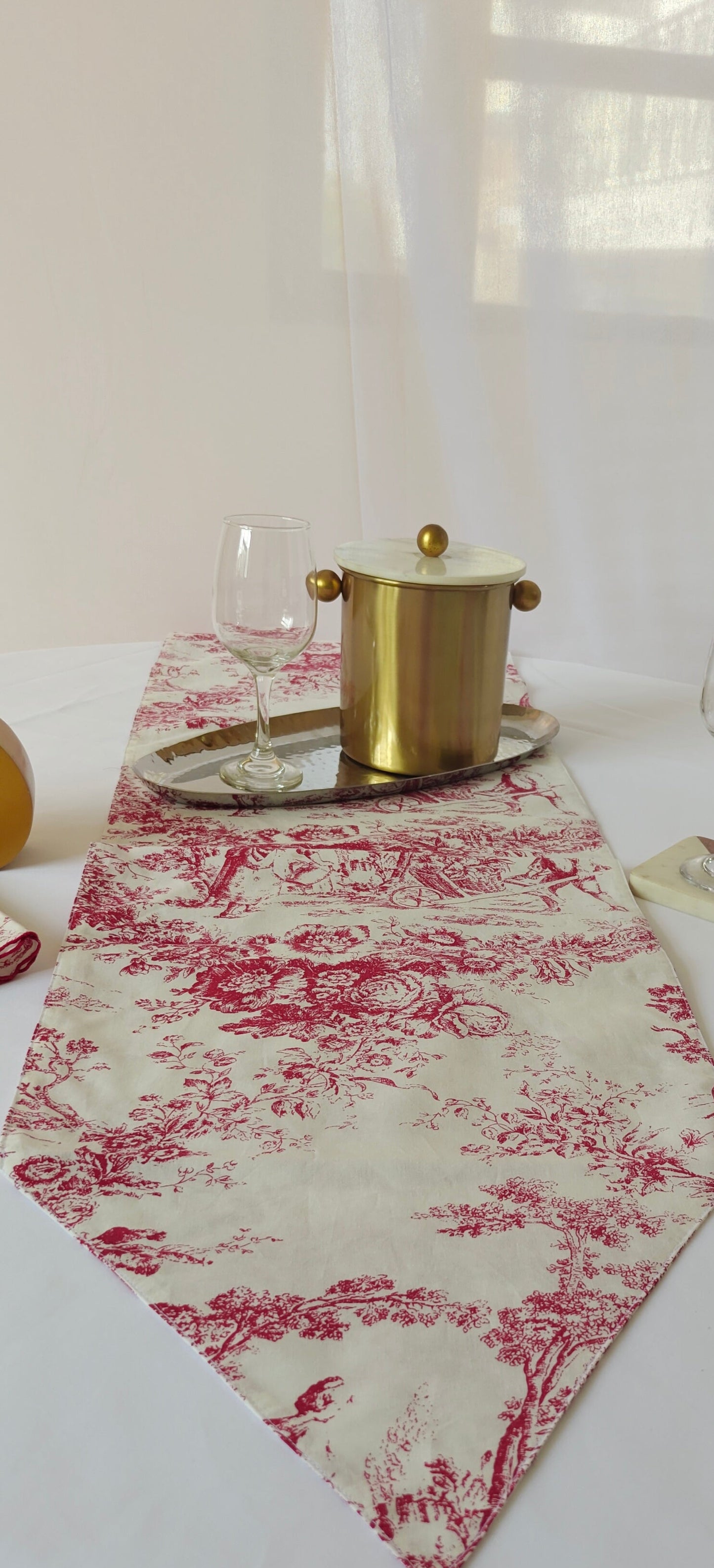Table setting with a red and white patterned table runner, glasses, and a pot.