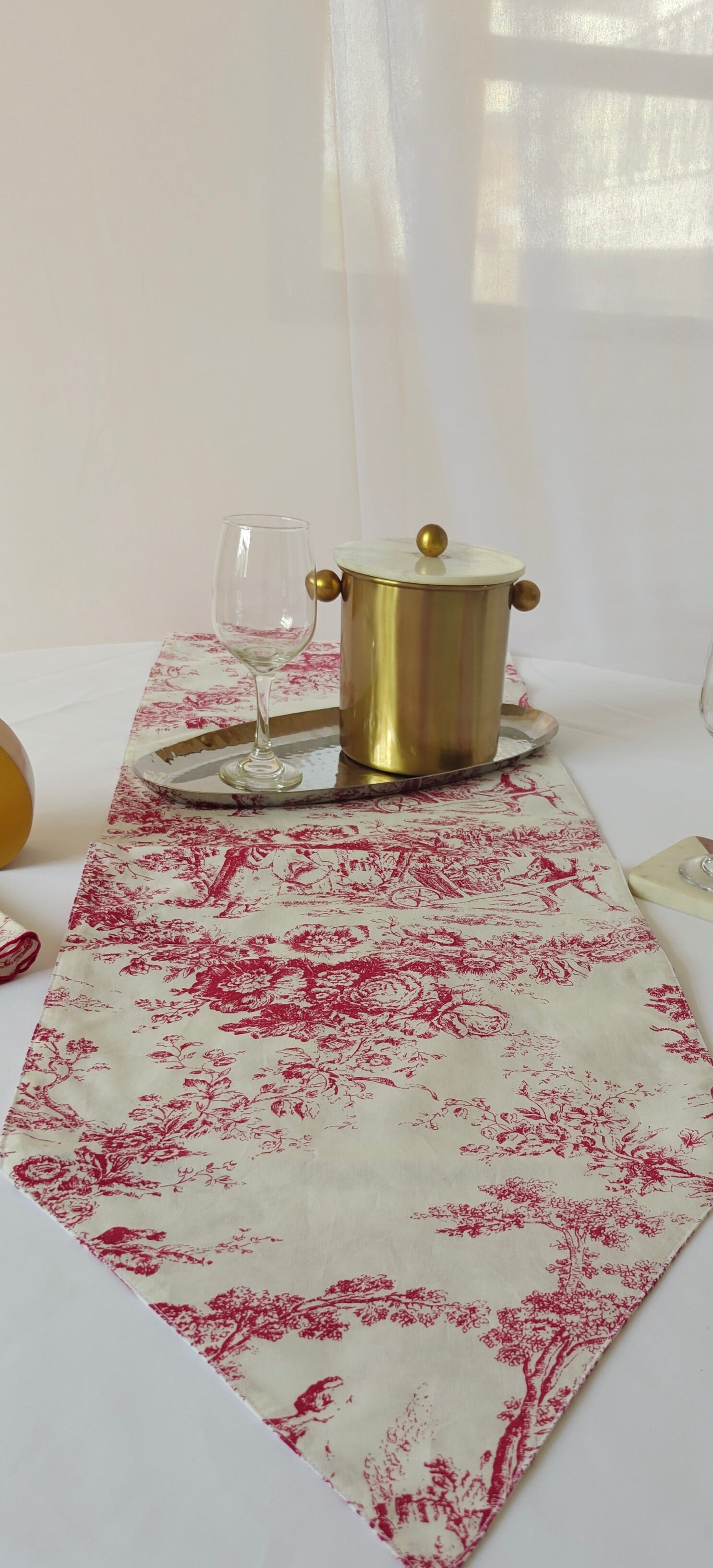 Table setting with a red and white patterned table runner, glasses, and a pot.