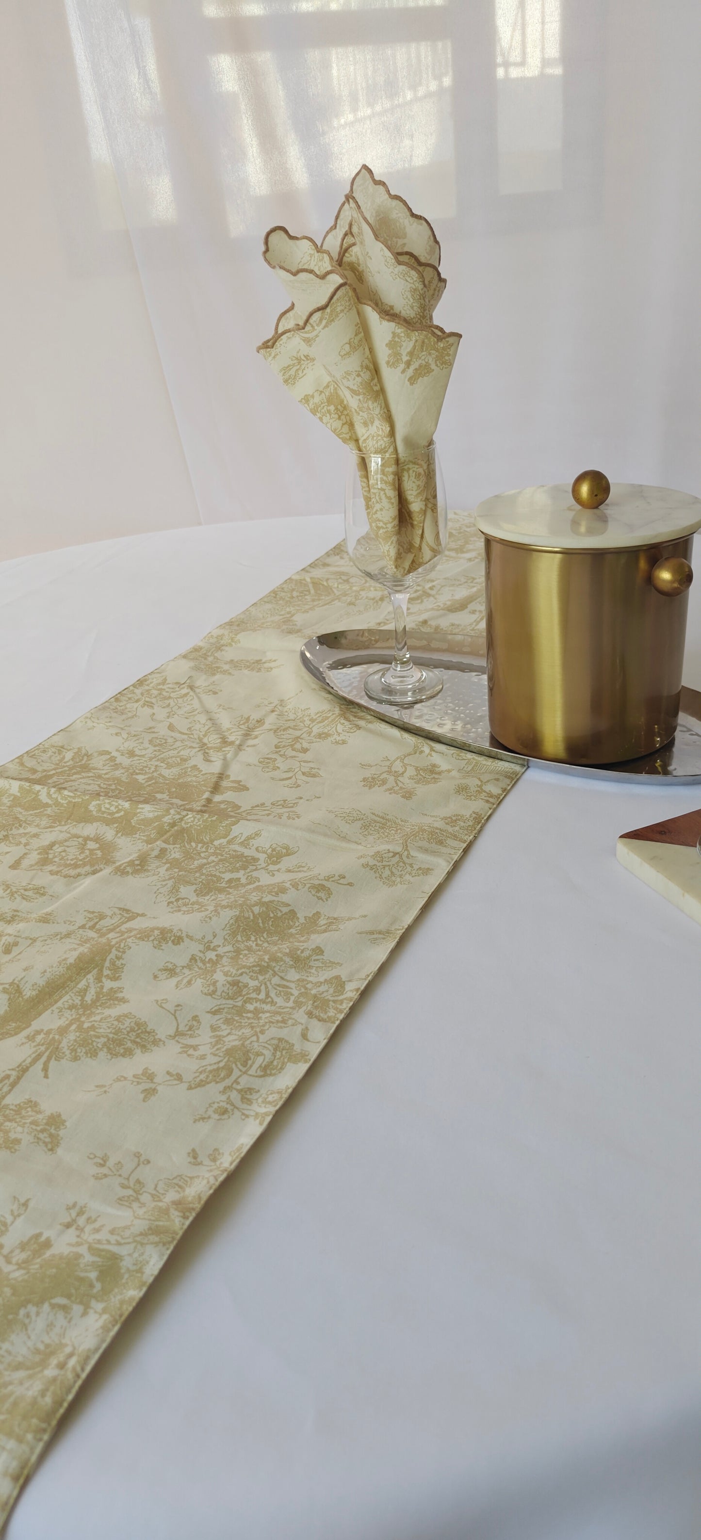 Decorative table setting with a gold vase, candle, and patterned runner on a white surface.