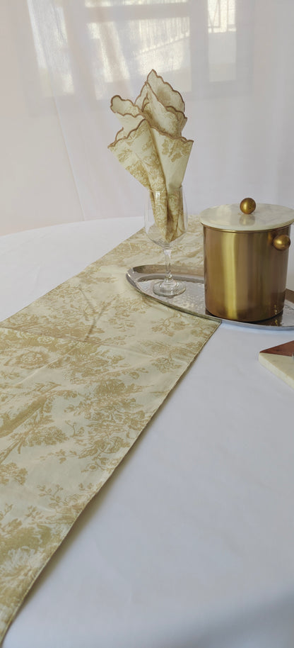 Decorative table setting with a gold vase, candle, and patterned runner on a white surface.