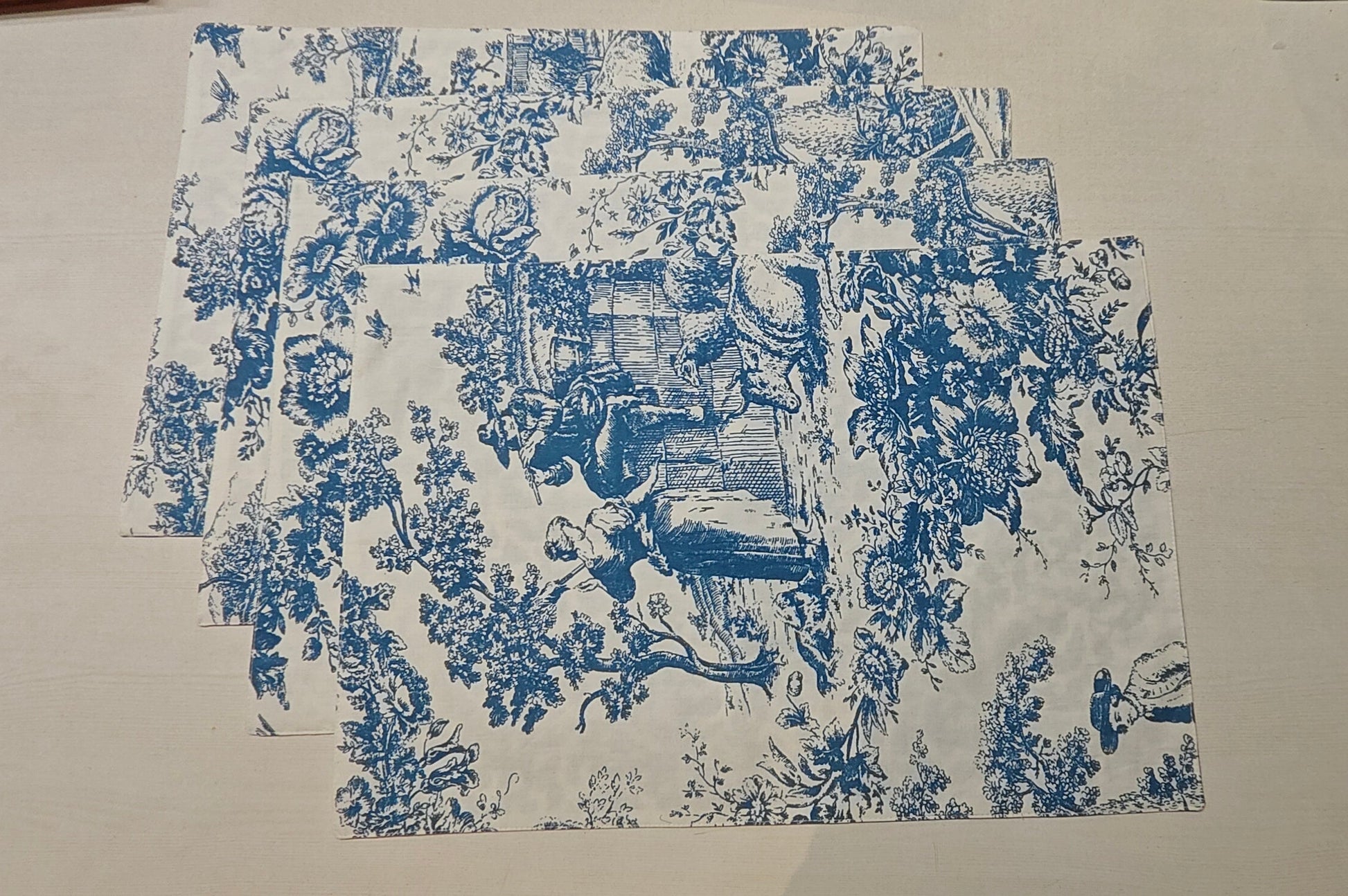 Set of blue and white toile-patterned placemats on a beige surface