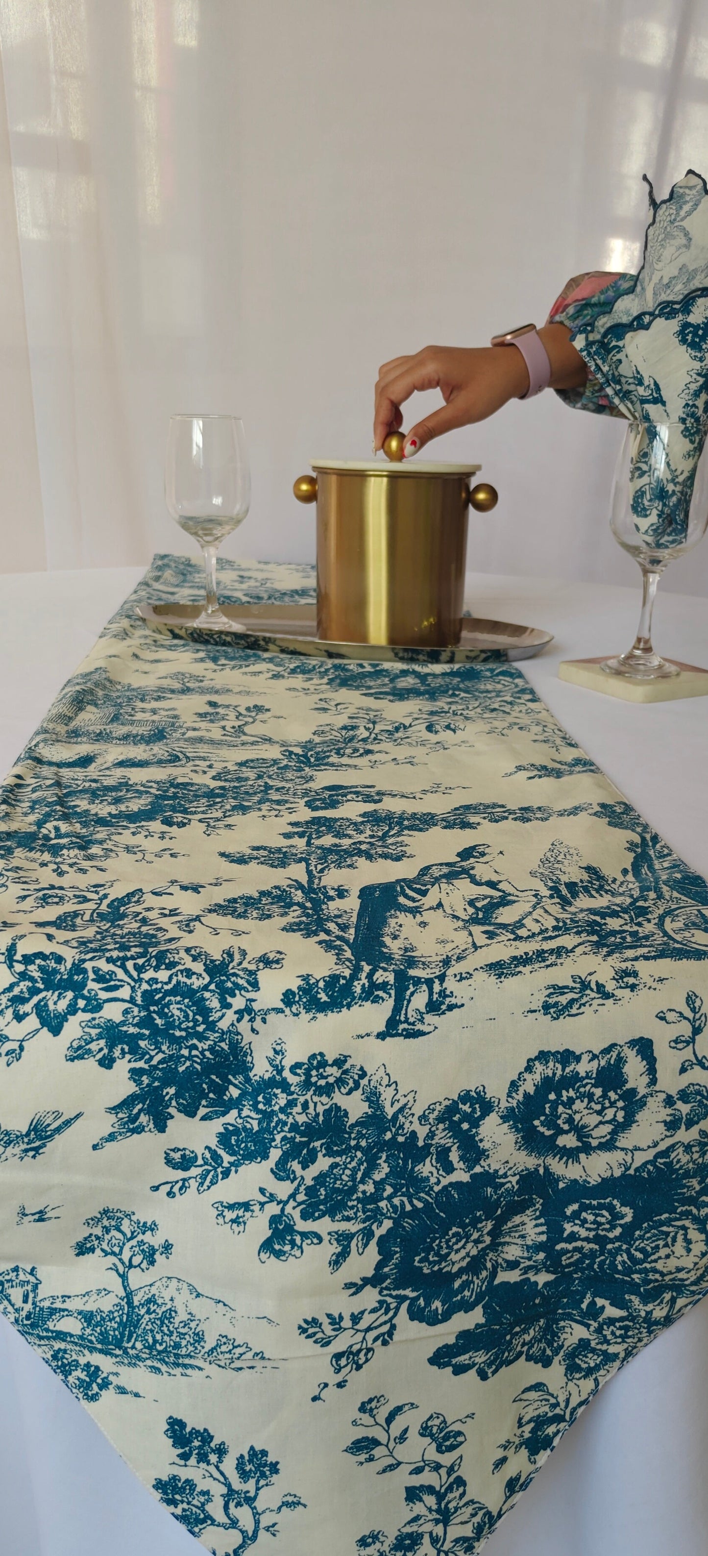 Table setting with a blue and white floral table runner, gold ice bucket, and wine glasses.