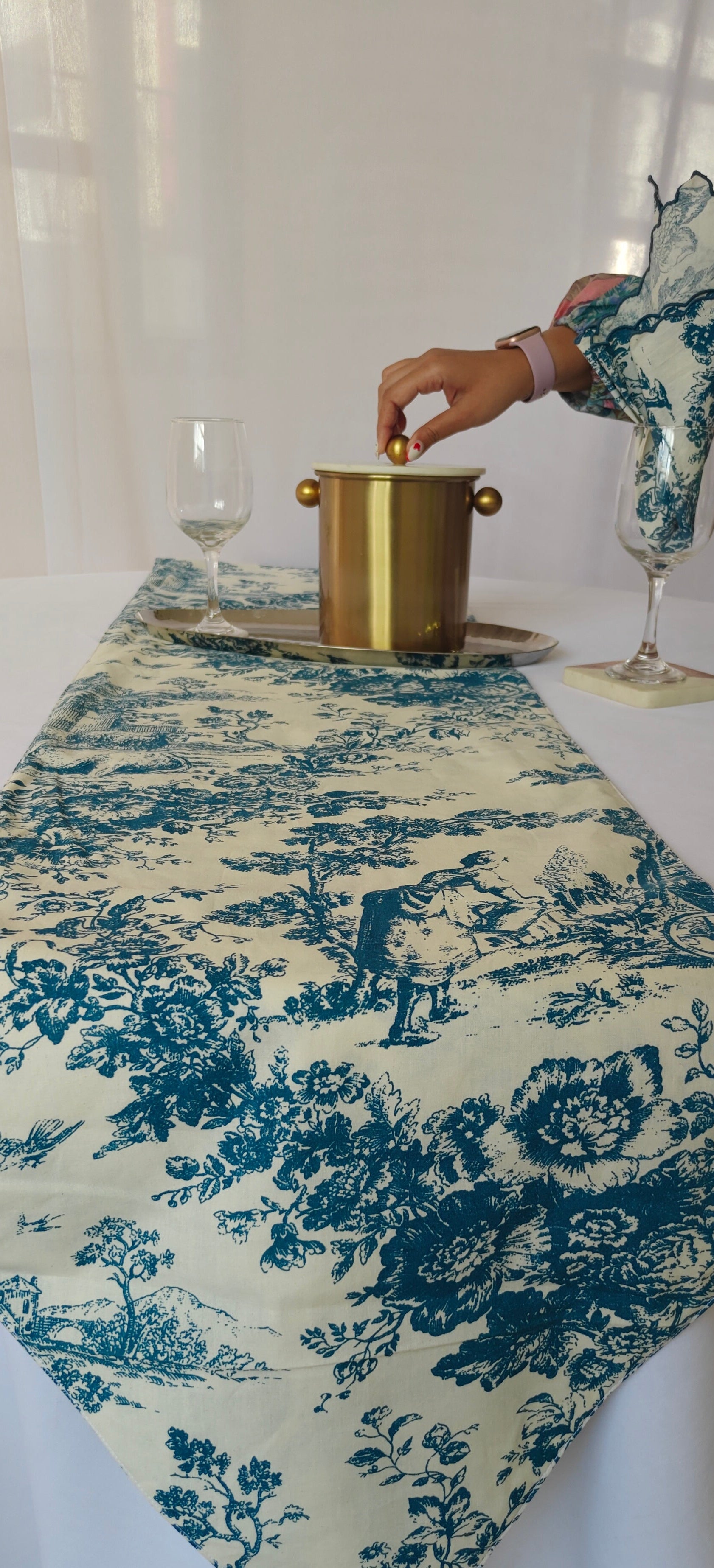Table setting with a blue and white floral table runner, gold ice bucket, and wine glasses.